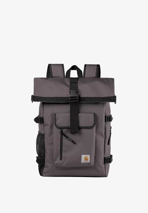 Mochila de tela gris con cierre de tipo roll-top, hebilla, bolsillo frontal y bolsillos laterales de malla. Cuenta con correas ajustables y un parche con el logo.