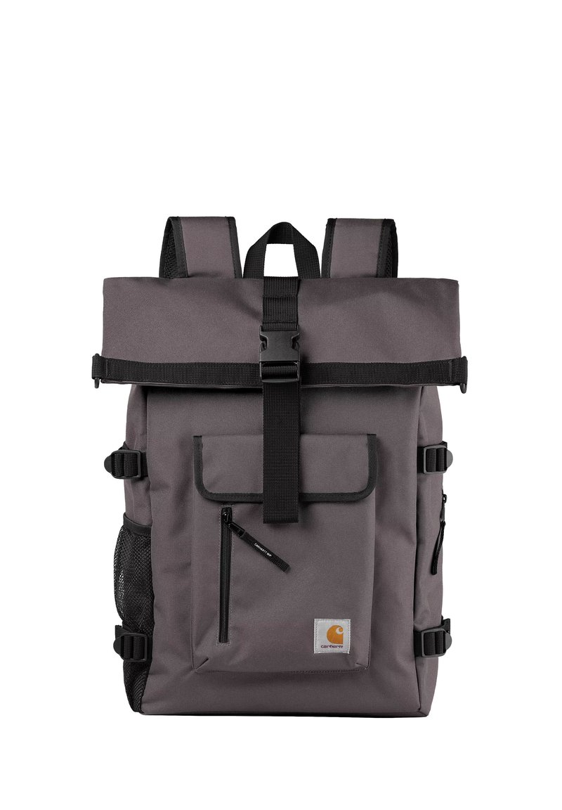 Mochila de tela gris con cierre de tipo roll-top, hebilla, bolsillo frontal y bolsillos laterales de malla. Cuenta con correas ajustables y un parche con el logo.