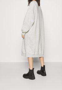 Vestido sudadera gris de gran tamaño con mangas largas y dobladillo acanalado, combinado con botas negras de tobillo gruesas. Textura suave, ajuste relajado.