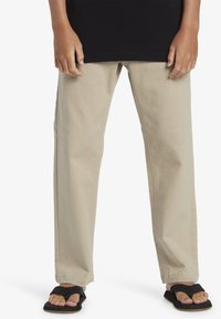 Beige rechtpijplijnen gemaakt van zachte stof, met een eenvoudig ontwerp en gecombineerd met zwarte flip-flops, wat de casual uitstraling benadrukt.