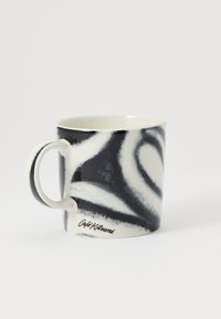 Taza de cerámica con un patrón de remolino en blanco y negro, textura suave, forma redondeada y asa blanca. Presenta la marca "Café Kitsuné".
