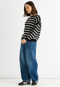 Black and white striped knit sweater with a round neckline, paired with loose blue denim jeans and black sneakers with white accents.