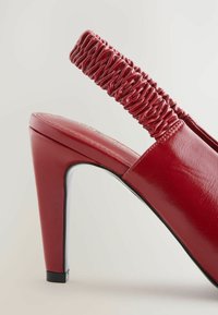 Rdeča visoka petka s slingback obliko in sijočo usnjeno površino, z nagubanimi trakovi na hrbtu in debelim, poševnim peto.