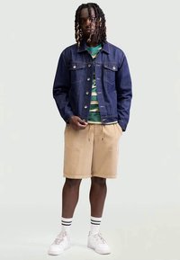 Denim jacket, green and striped t-shirt, beige corduroy shorts, white sneakers with black stripes, and a relaxed fit.