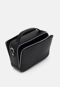 Sac en cuir noir avec une fermeture éclair argentée contrastante, de forme rectangulaire, deux compartiments, une poignée robuste et un design minimaliste.