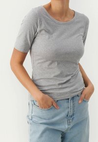 Grijze t-shirt met korte mouwen gemaakt van zachte stof, met een ronde halslijn en een aansluitend ontwerp. Gepaard met lichtblauwe spijkerbroek.