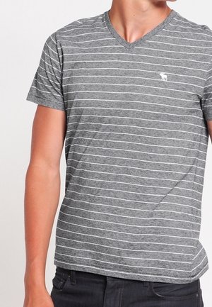 Man wearing a grey V-neck T-shirt with thin horizontal white stripes and a small white animal logo on the chest.
