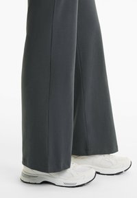 Graue weit geschnittene Hosen fallen über weiße Sportschuhe und zeigen ein lässiges Outfit, das Komfort und Stil in den Vordergrund stellt.