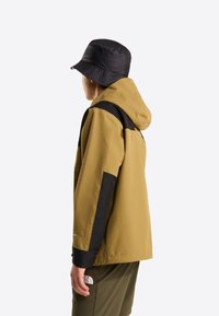 Hættetrøje i gulbrun med sorte detaljer og ærmer; glat tekstur; kombineret med en sort bøllehat; båret med grønne shorts.