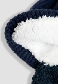 Tumesinine pusa, millel on valge, pehme fliisvooder. Omab sooniktekstuuriga äärist ja on pehme ning mugav.