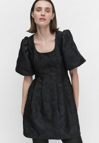 Svart klänning med ett strukturerat blomster mönster, korta puffärmar, fyrkantig halsringning och en figurnära överdel med en utsvängd kjol.