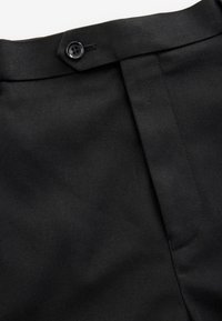 Ceinture en tissu noir avec un bouton noir et une braguette zippée cachée sur un pantalon.