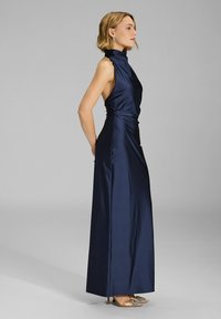 Navy blue satin gown with high collar, sleeveless design, and draped waist. A long silhouette with subtle sheen and elegant texture.