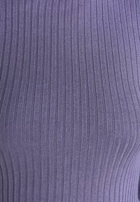 Gros plan de tissu tricoté côtelé violet avec des lignes texturées verticales créant un motif rayé.