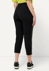 Zwarte tapered joggers van een gestructureerde stof, met een levendige groene streep langs de zijkant, een elastische tailleband en een cropped lengte.