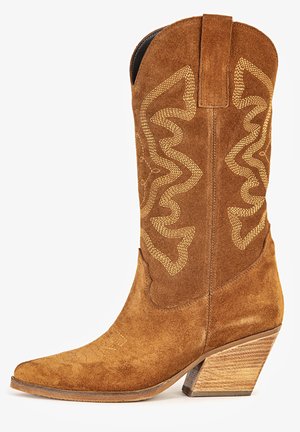 Bota de vaquero de ante marrón con costuras decorativas, punta puntiaguda, tira para tirar y tacón de madera apilada inclinado.