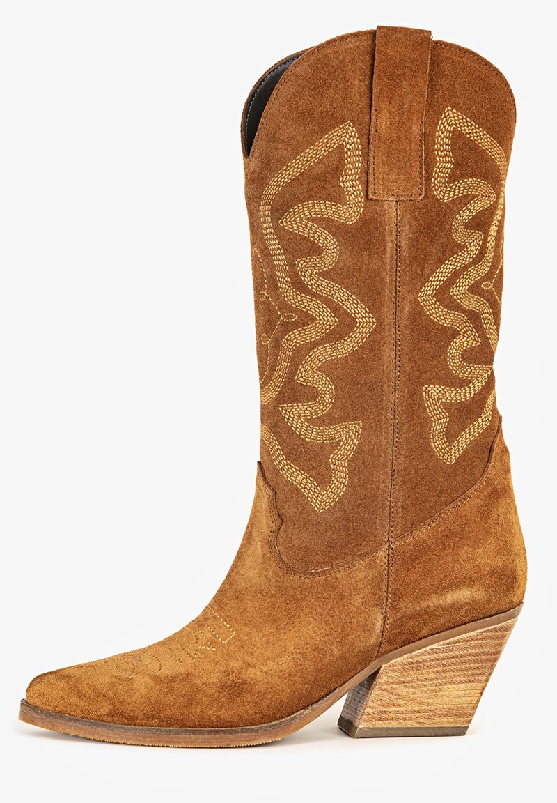 Botte de cowboy en daim marron avec coutures décoratives, bout pointu, languette de préhension et talon en bois empilé incliné.