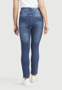Siniset korkeavyötäröiset skinny farkut, joissa on sileä denim-pinta, kahdella takataskulla ja kapealla leikkauksella, yhdistettyinä valkoisiin tennareihin.