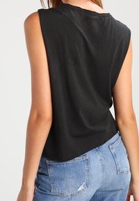 Mustat ilmanhihoja oleva toppi, jossa on rento leikkaus ja hieman kaareva helma, yhdistettynä vaaleansinisiin kulutettuihin farkkuroggeihin.