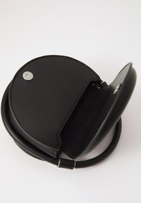 Sac circulaire noir en cuir avec une texture lisse, fermeture magnétique, bandoulière détachable et un compartiment intérieur spacieux.