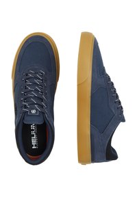 Zapatillas de tela azul oscuro con suelas de goma marrón, cordones blancos y adornos de logo. Presenta una superficie texturizada y un diseño de puntera redondeada.