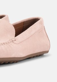 Μαλακό μοκασίνι από ροζ σουέντ με στρογγυλεμένη μύτη, σχεδιασμό χωρίς κορδόνια και καφέ λαστιχένια σόλα με εξογκώματα για καλύτερη πρόσφυση.