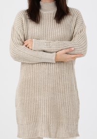 Robe-pull beige en tricot avec col montant, coupe ample, poignets côtelés et texture épaisse. Se termine au-dessus des genoux, avec une silhouette droite.