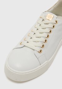 Weiße Ledersneaker mit gerippter Gummisohle, goldenen Ösen und cremefarbenen Schnürsenkeln. Verfügt über ein dezentes Logo auf der Zunge und eine glatte Textur.
