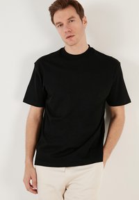 Tricou din bumbac negru cu mâneci scurte, guler rotund și croială lejeră. Textură netedă, design minimalist, fără modele sau accente vizibile.
