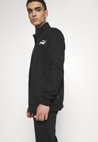 Black athletic jacket with zip closure, high collar, soft texture, and white Puma logo on the left chest. Slim fit design with ribbed cuffs.