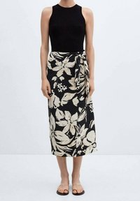 Top in cotone nero a costine abbinato a una gonna lunga fino alla caviglia con stampa floreale in crema e nero. La gonna presenta un dettaglio con nodo laterale e un tessuto leggero e fluido.