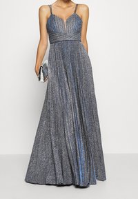Glittrig blå aftonklänning med plisserad design, v-ringning och tunna axelband. Pairad med en silverclutch.