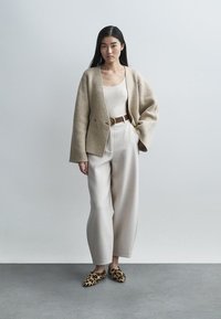 Béžový vlnený kardigán, biele tielko, krémové široké nohavice, hnedý opasok a leopardie slip-on topánky. Jemné textúry, uvoľnený strih.