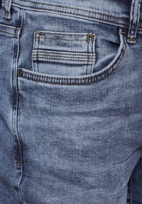 Blå denimjeans med en urtvättad struktur, femfickdesign, synlig sömnad och en knapp på bakfickan.