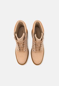 Beige tursko laget av semsket skinn med en glatt tekstur, med metalløyer, runde snører og en robust gummisåle.