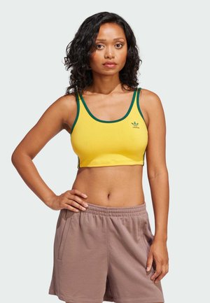 Cropped top amarillo con ribete verde y pequeño logo, combinado con pantalones cortos marrón claro que cuentan con una cinturilla elástica y bolsillos laterales.