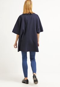 Námořnická oversized tunika s krátkými rukávy, texturovaná látka a rovný střih, nošena přes slim džíny v modré barvě a černé boty.