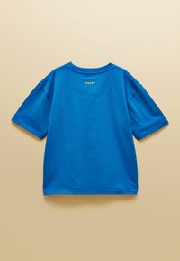 T-shirt à manches courtes bleu vif avec le logo "JOULES" imprimé près de l'encolure à l'arrière sur un fond beige.