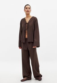 Rjava, ohlapna bombažna obleka z širokim V-neck vrhom s trakom in širokimi hlačami. Gladka tekstura in sproščen silhuet.