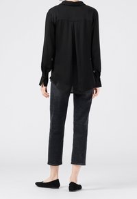 Svart långärmad skjorta med krage, genomskinligt tyg, detalj med veck bak; matchad med mörkgrå jeans och svarta platta skor.