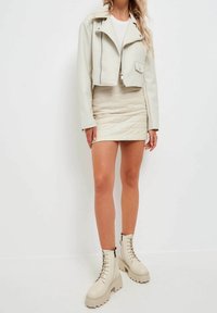 Chaqueta de cuero recortada color beige claro, falda acolchada ajustada color crema y botas beige con cordones gruesos y suelas gruesas.