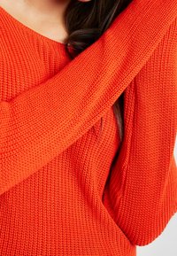 Maglione leggero a maglia di un vivace rosso con un motivo texturizzato, dotato di un ampio scollo e maniche lunghe per una vestibilità rilassata.