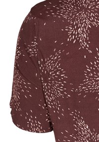 Bruine top met korte mouwen, gemaakt van een textuurstof met een wit abstract patroon dat lijkt op kleine ovalen die over het oppervlak zijn verspreid.
