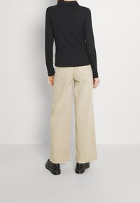 Schwarzes langärmliges Poloshirt mit Kragen, kombiniert mit beigen weit geschnittenen Hosen. Schwarze klobige Schuhe runden das Outfit ab. Glatte Stoffstruktur.