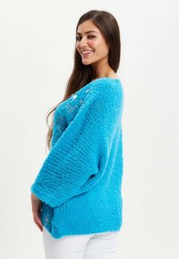Bright blue oversized knit sweater with a textured, fluffy fabric and open knit design. Features a ribbed hem and loose, wide sleeves.