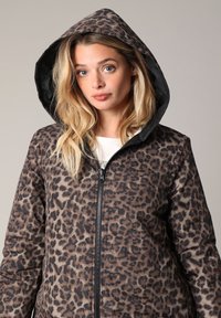 Veste à imprimé léopard avec capuche noire, dotée d'une fermeture éclair et de manches longues, fabriquée en tissu lisse avec un léger éclat.