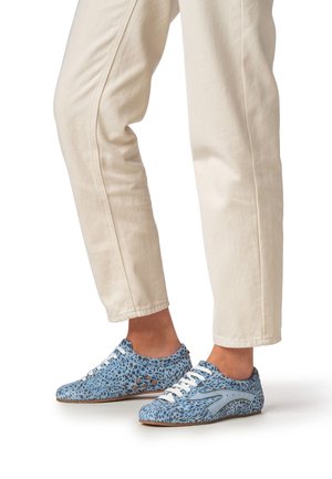 Blauwe schoenen met luipaardprint van een gestructureerde stof, witte veters en een bruine rubberen zool, gecombineerd met beige broek.