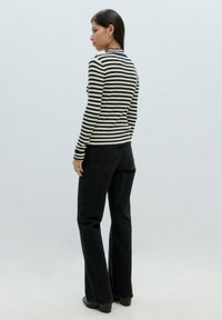 Gestreiftes Rippenoberteil mit langen Ärmeln in Schwarz und Weiß, kombiniert mit schwarzen Schlagjeans. Das Model wird von hinten gezeigt und steht vor einem hellen Hintergrund.