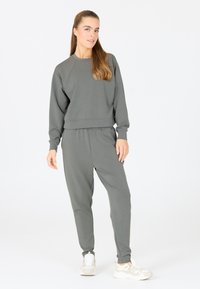 Grå sweatshirt och joggers-set. Sweatshirt har raglanärmar och rundad halsringning. Joggers har elastisk midja och avslutade anklar.