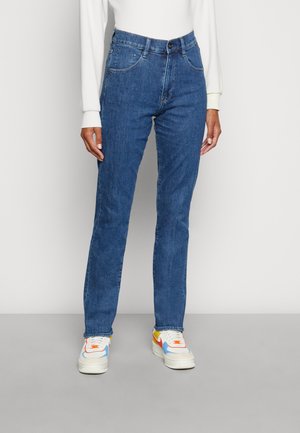 Blue denim jeans featuring a straight-leg cut, five pockets, and top-stitch detailing, paired with multicolored athletic sneakers.